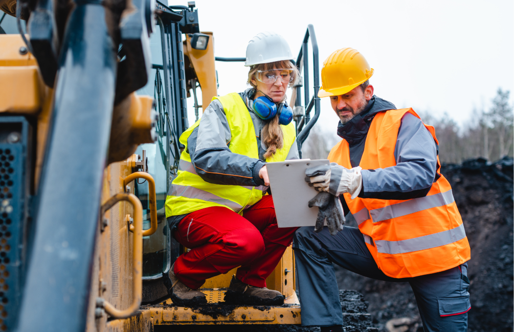 Two mining staff discussing at mine site with equipment next to them